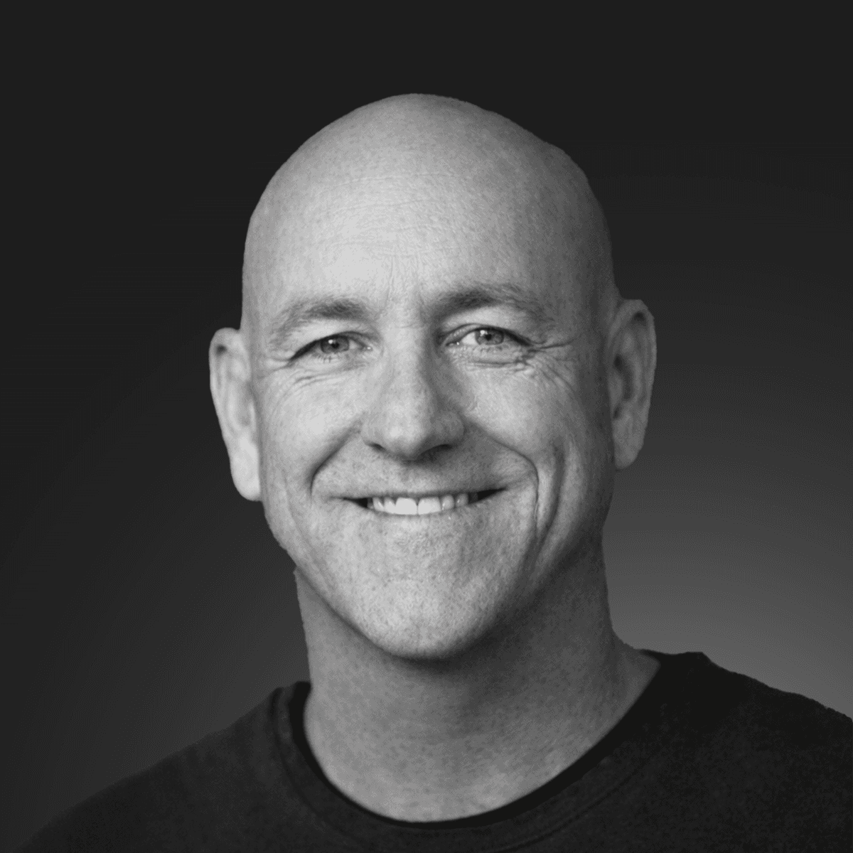 A smiling person with curly hair, wearing a leather jacket, stands in a cozy indoor setting.