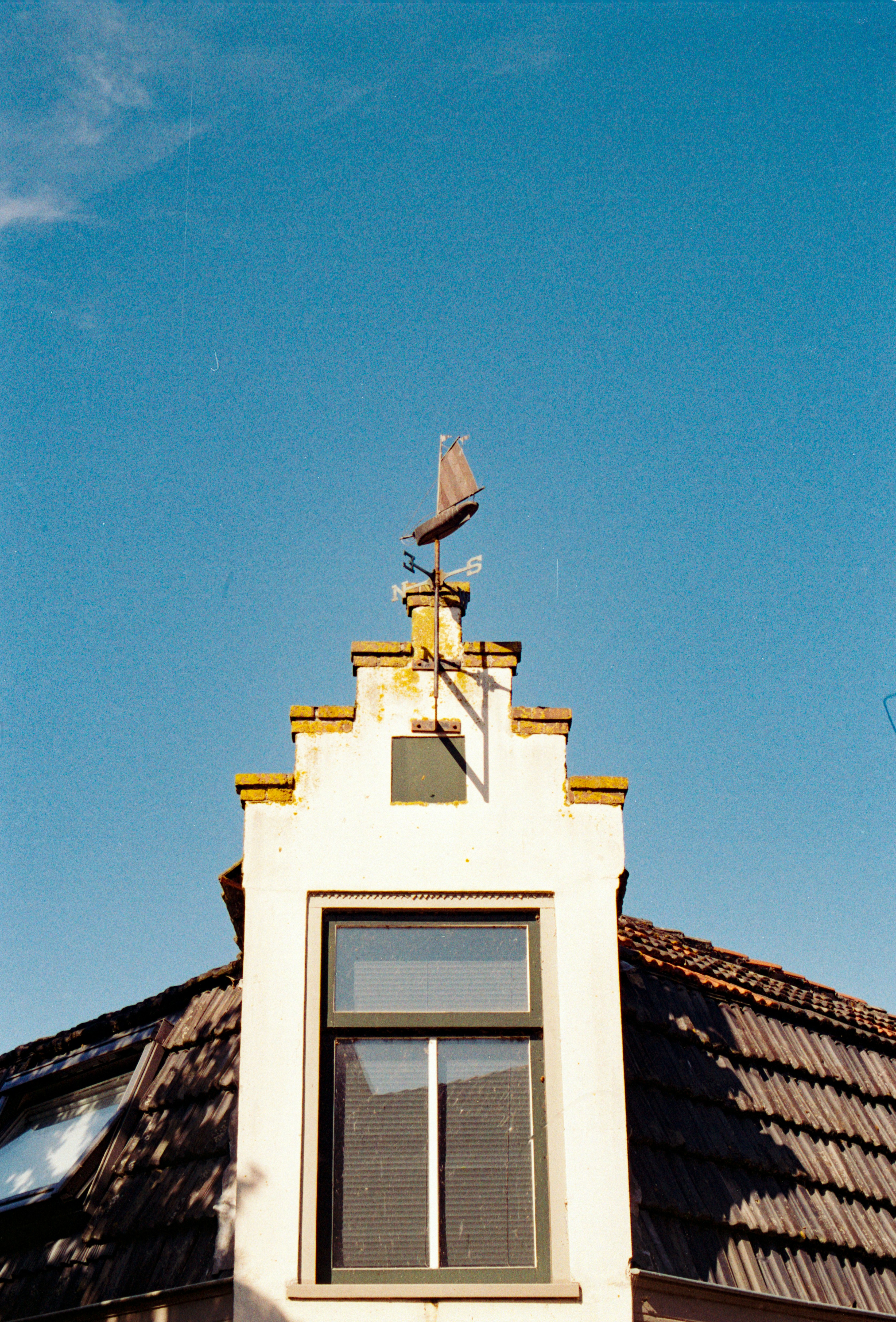 White building facade with a weather vane against blue sky