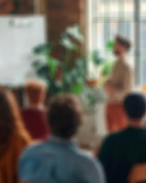 Rozostřený záběr lidí na workshopu. Ilustrace živé spolupráce a dialogu s komunitami.
