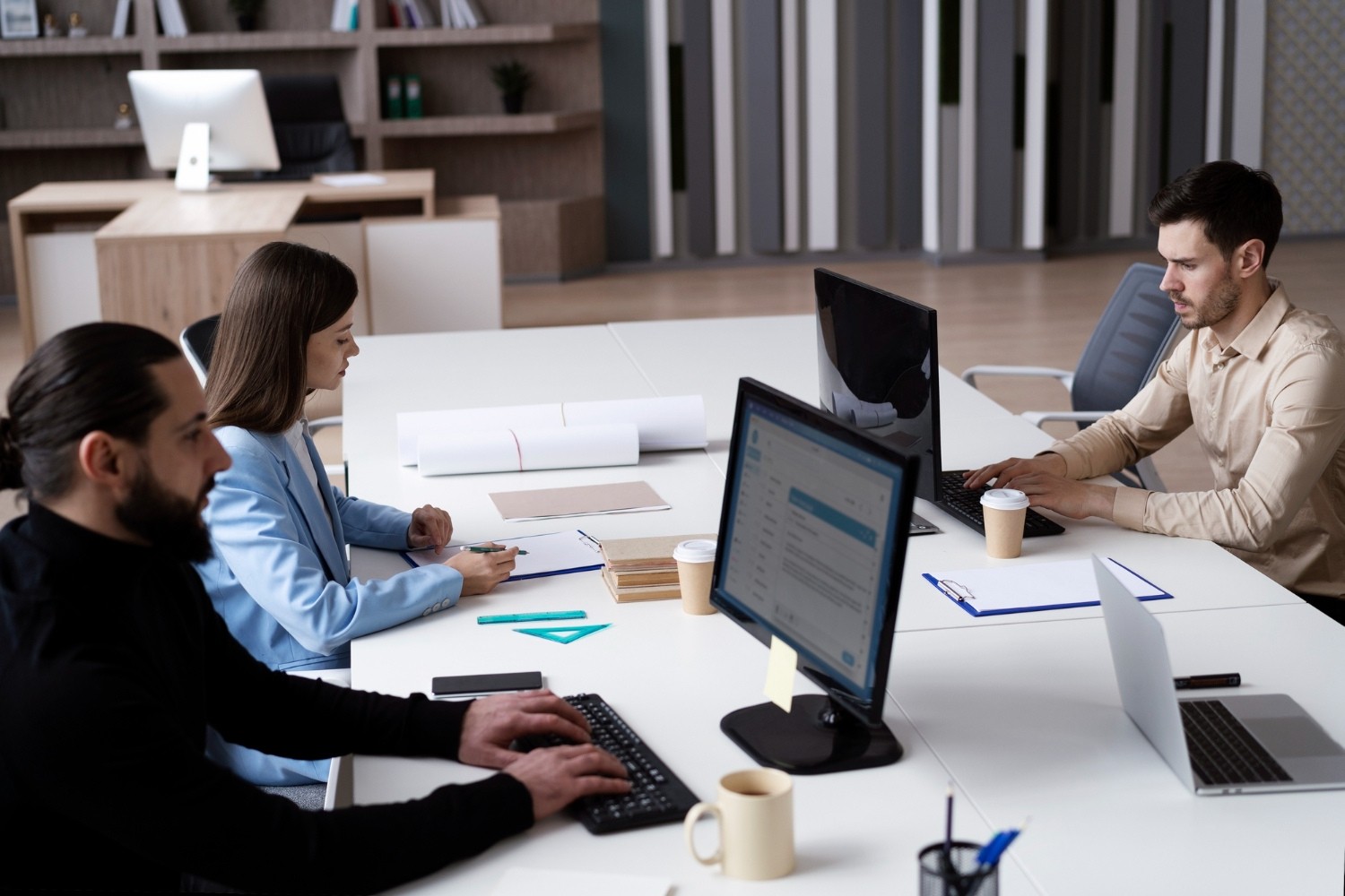 three people sitting on a desk in front of their computers in a meeting room