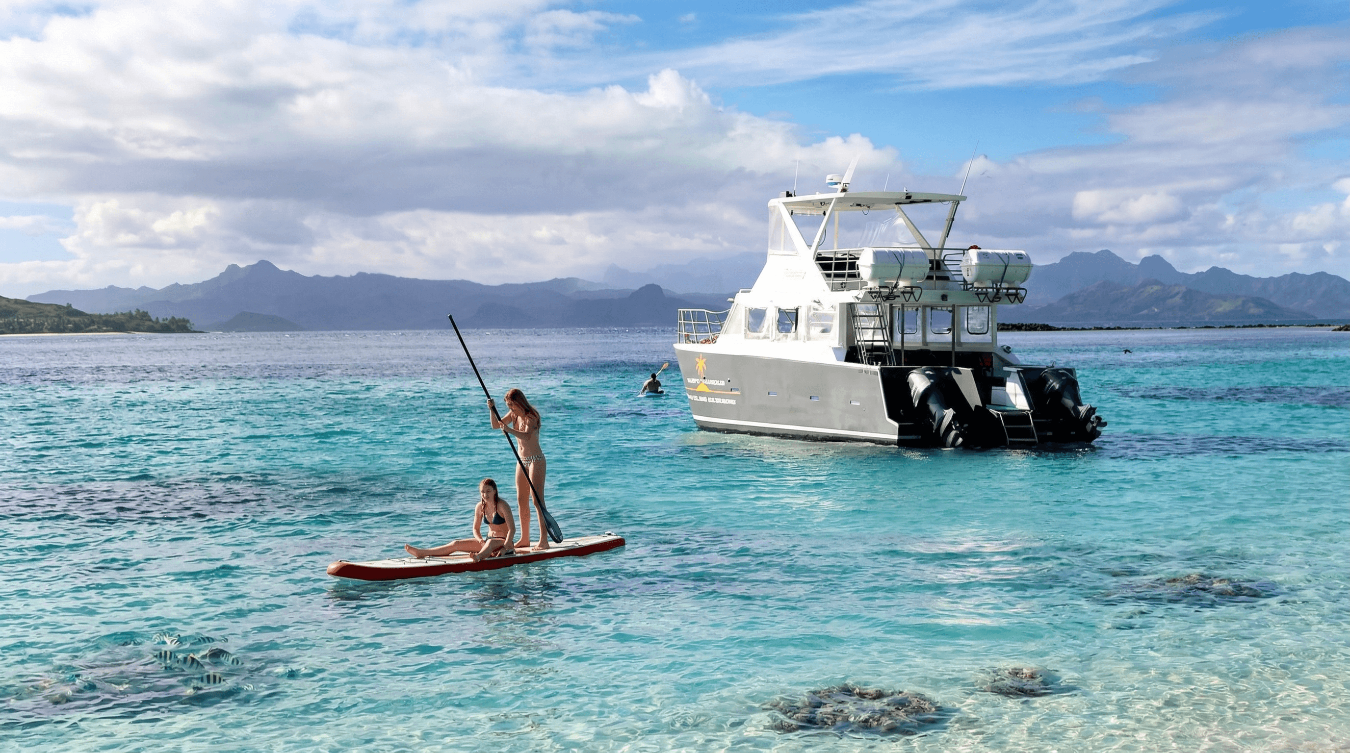 Two girls on paddle boards with a boat in the background on Pacific Harbour Fiji