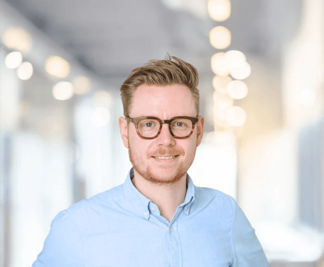 Dennis Meyer Philippi, Geschäftsführer von Tantum Sana, Portrait eines Mannes mit Brille im hellblauen Hemd vor modernem Bürohintergrund.