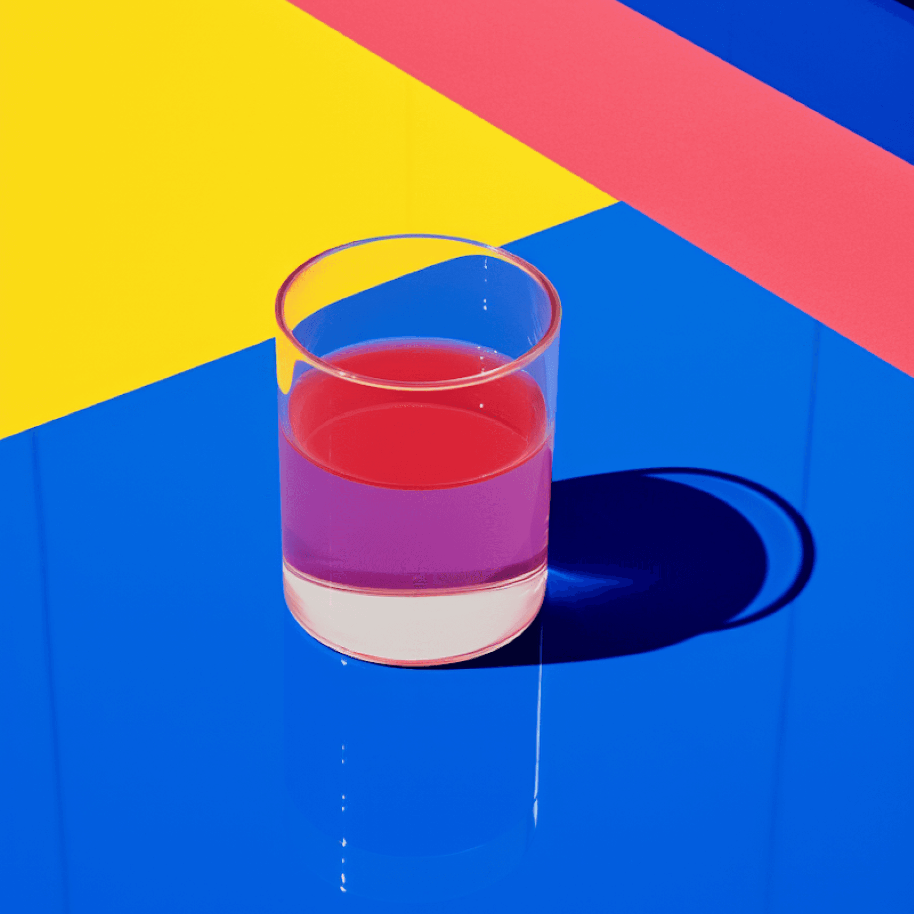 Glass of pink liquid on a glossy blue surface with yellow and pink diagonal bands above