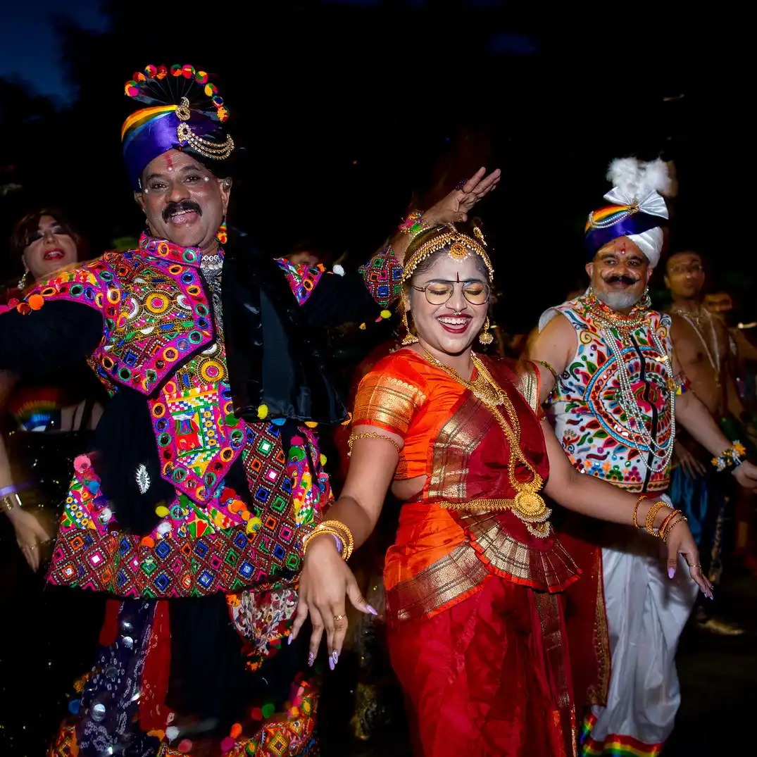 People in colorful traditional Indian attire dance joyfully at night, displaying vibrant patterns and accessories, exuding a festive and celebratory mood.