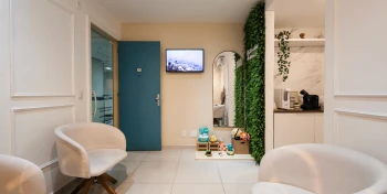 Sala de espera moderna e acolhedora da Nahser Odontologia no Rio de Janeiro, com poltronas brancas, parede verde e recepção minimalista.