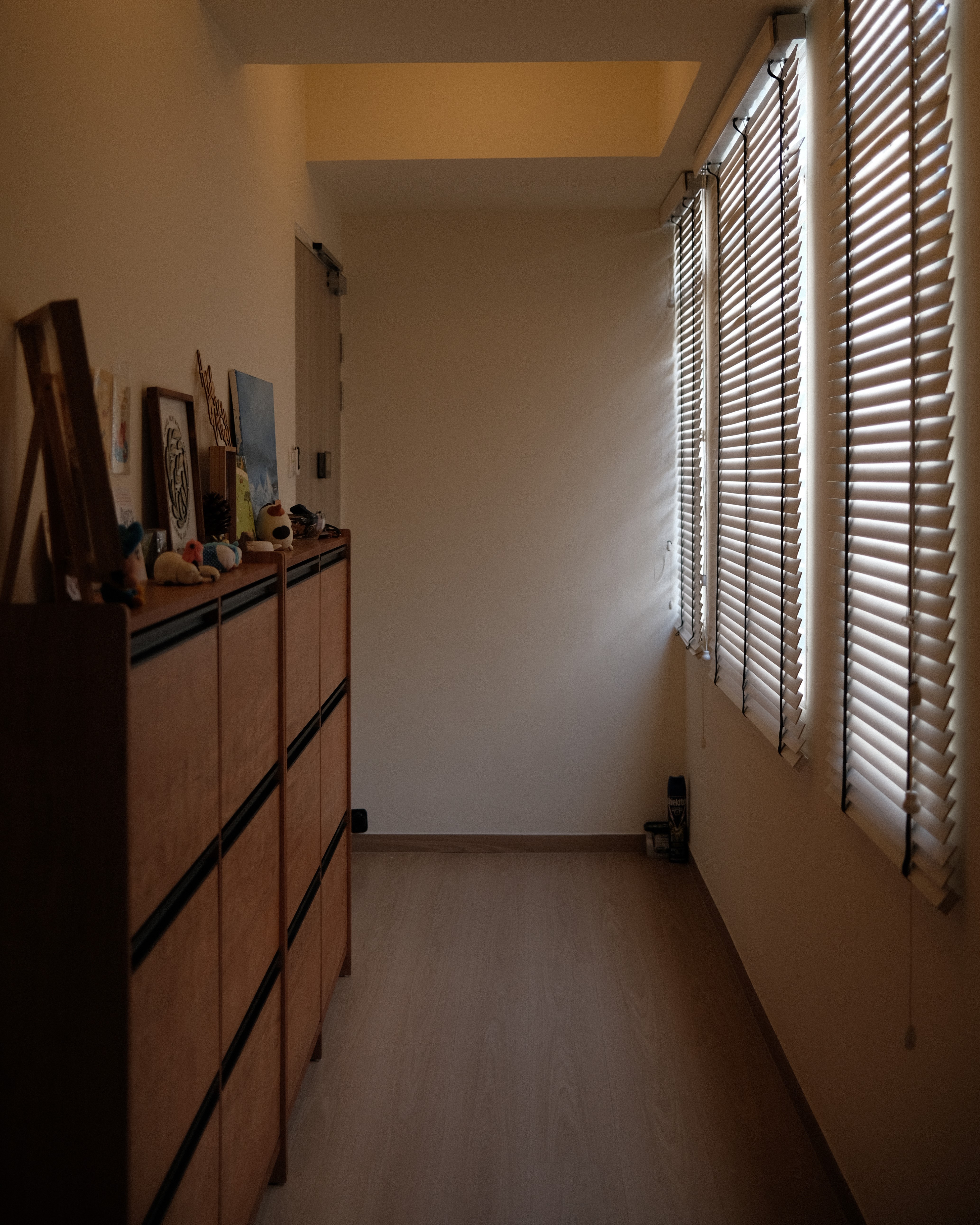 Entryway of Satu-Circle showcasing tall wooden cabinets, decorative art, and sunlight streaming through Venetian blinds, highlighting the apartment’s serene design.