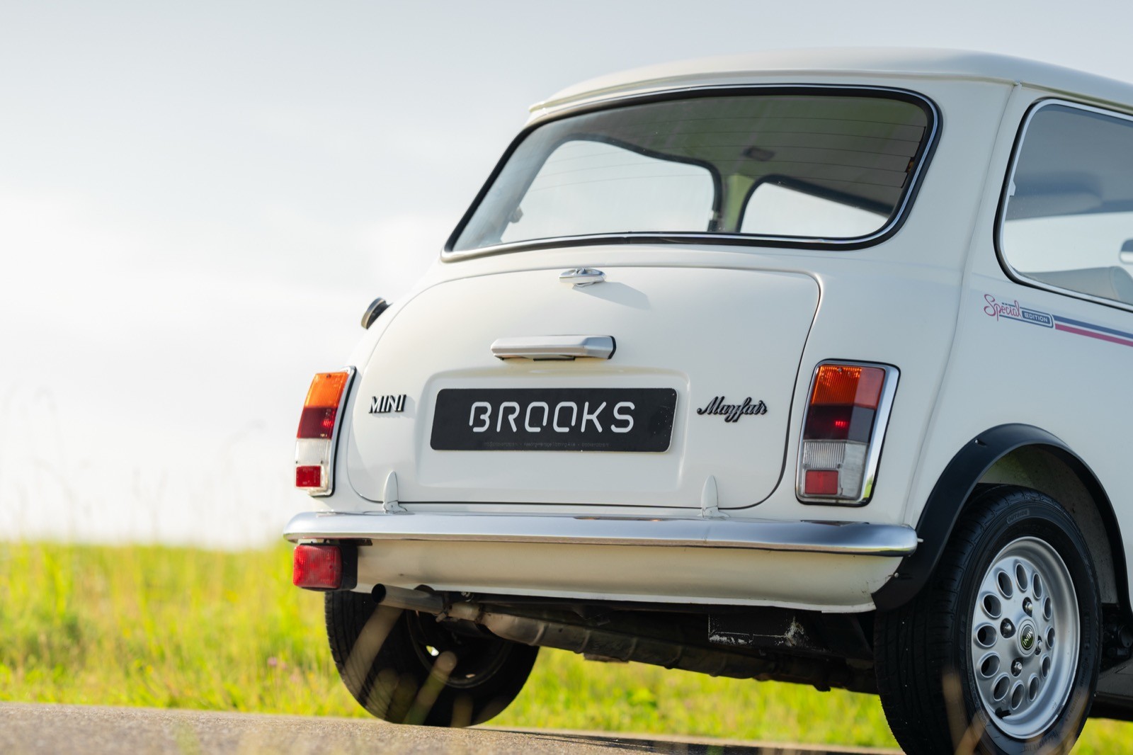 A classic white car parked on a road, with a grassy field in the background under a clear sky.