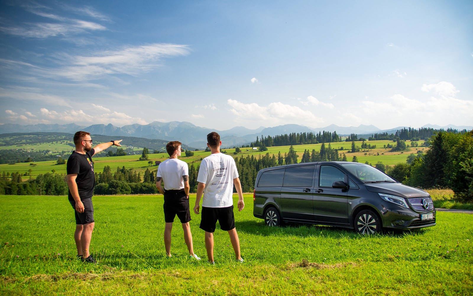 Tourists in a field near Zakopane with a van, enjoying mountain views.