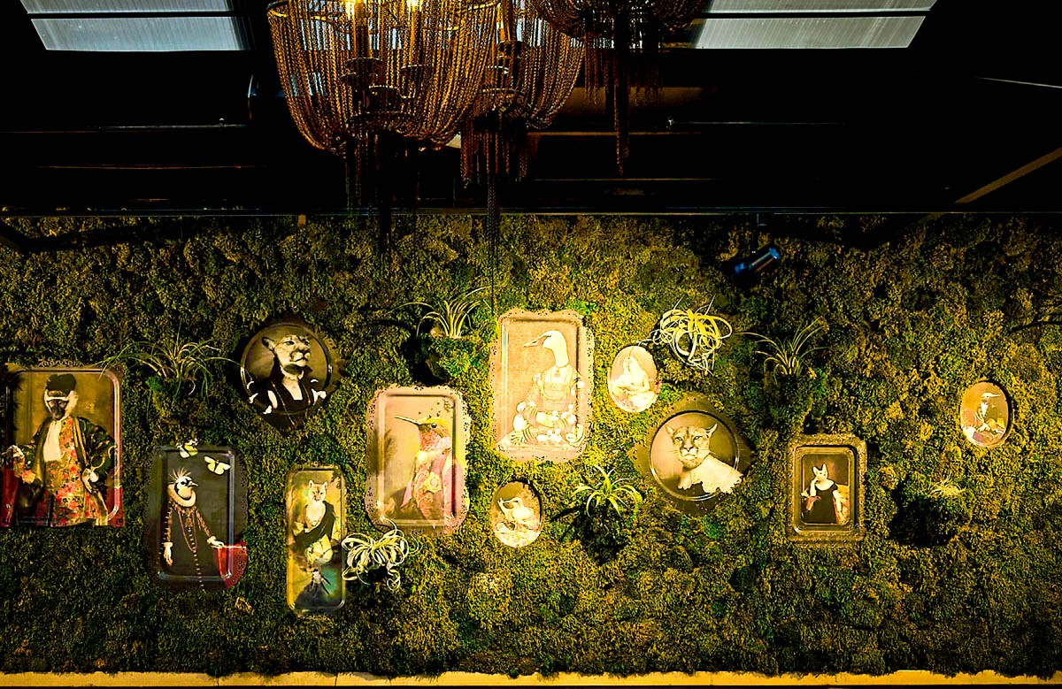 a grassy wall with a electic victorian artwork with animals hanging in the shrubs