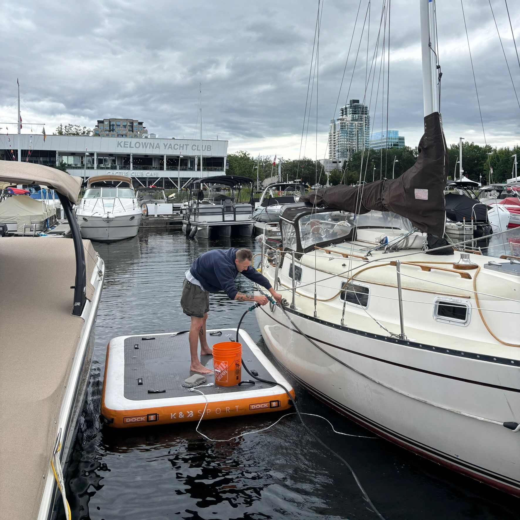 A man working on an inflatable dock to clean the side of a sailboat at a Kelowna marina