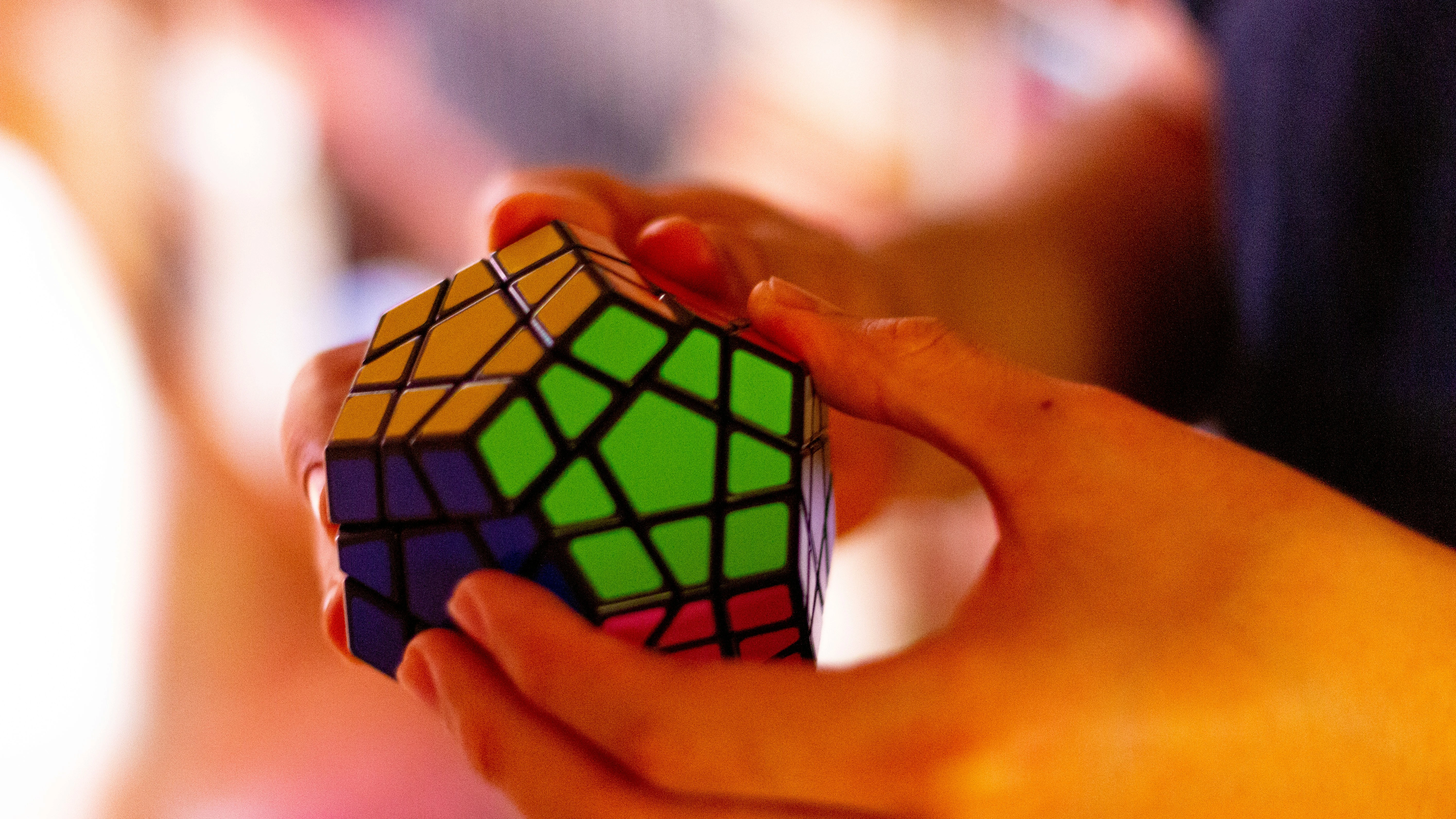 Close-up of hands solving a colorful Megaminx puzzle, showcasing focus and problem-solving skills in a bright, engaging environment.