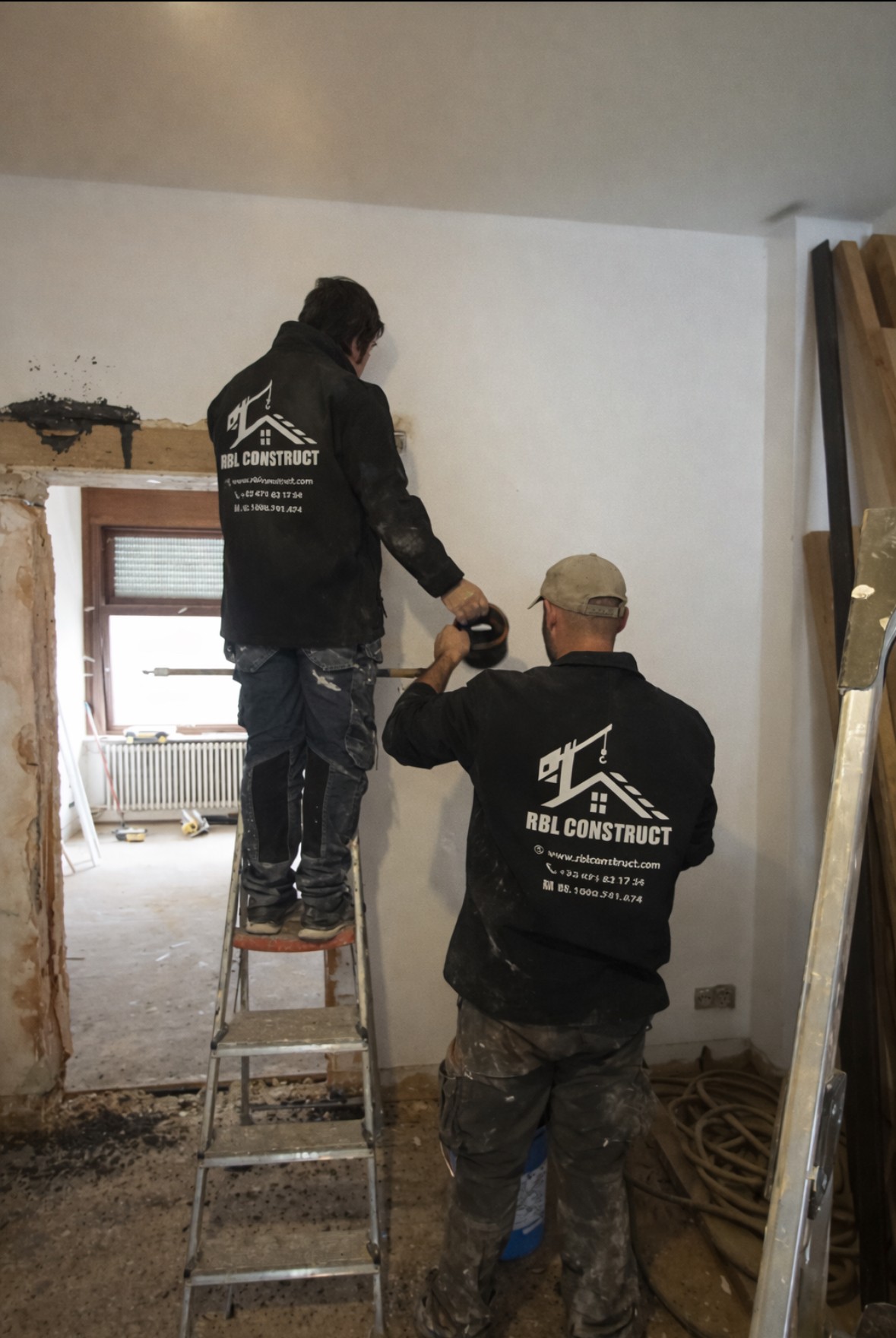 A serene outdoor seating area with two chairs, surrounded by lush greenery and a glassed-in structure.