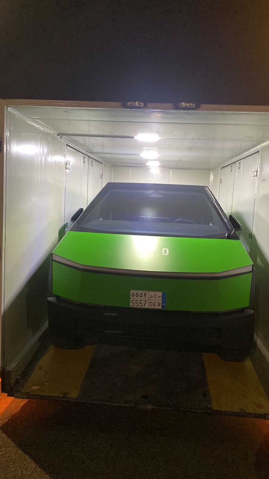 A bright green Tesla Cybertruck is placed inside an enclosed vehicle shipping haulier on a marked ramp. It is prepared for delivery.