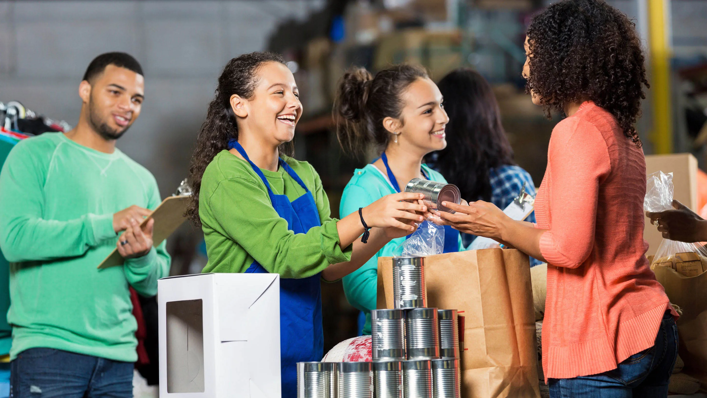 Teenage students at a food bank smiling as they serve food to community members, showcasing teamwork, service, and compassion during a volunteer activity.