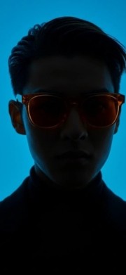 Ein Mann der eine orangene Brille trägt. Hintergrund ist grell blau