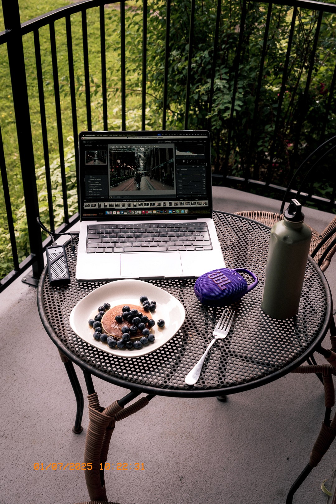 Pancakes aux bleuets, laptop et gourde sur une table de balcon.