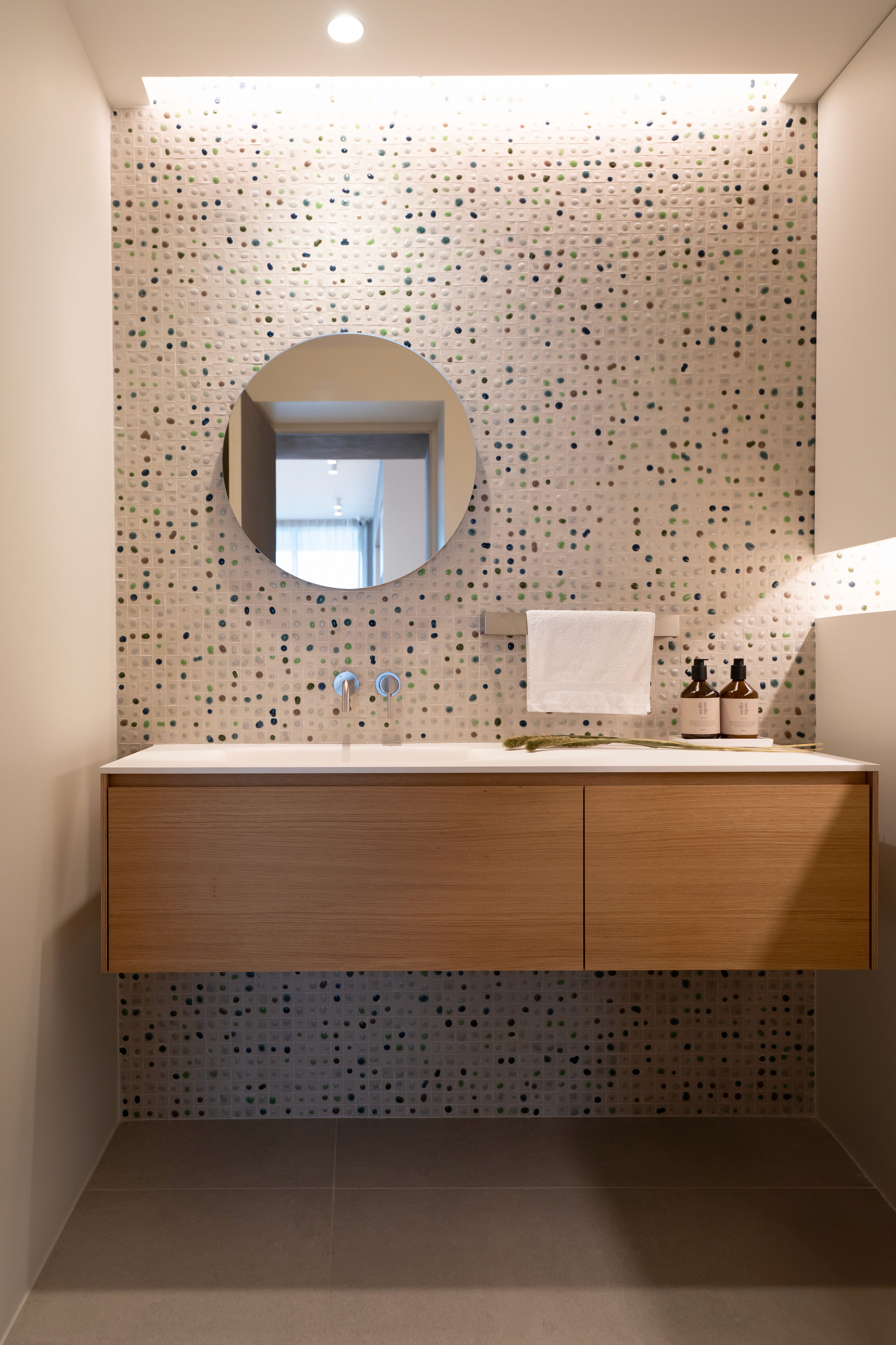 Baño moderno con azulejos irregulares en tonos verdes y mueble de madera