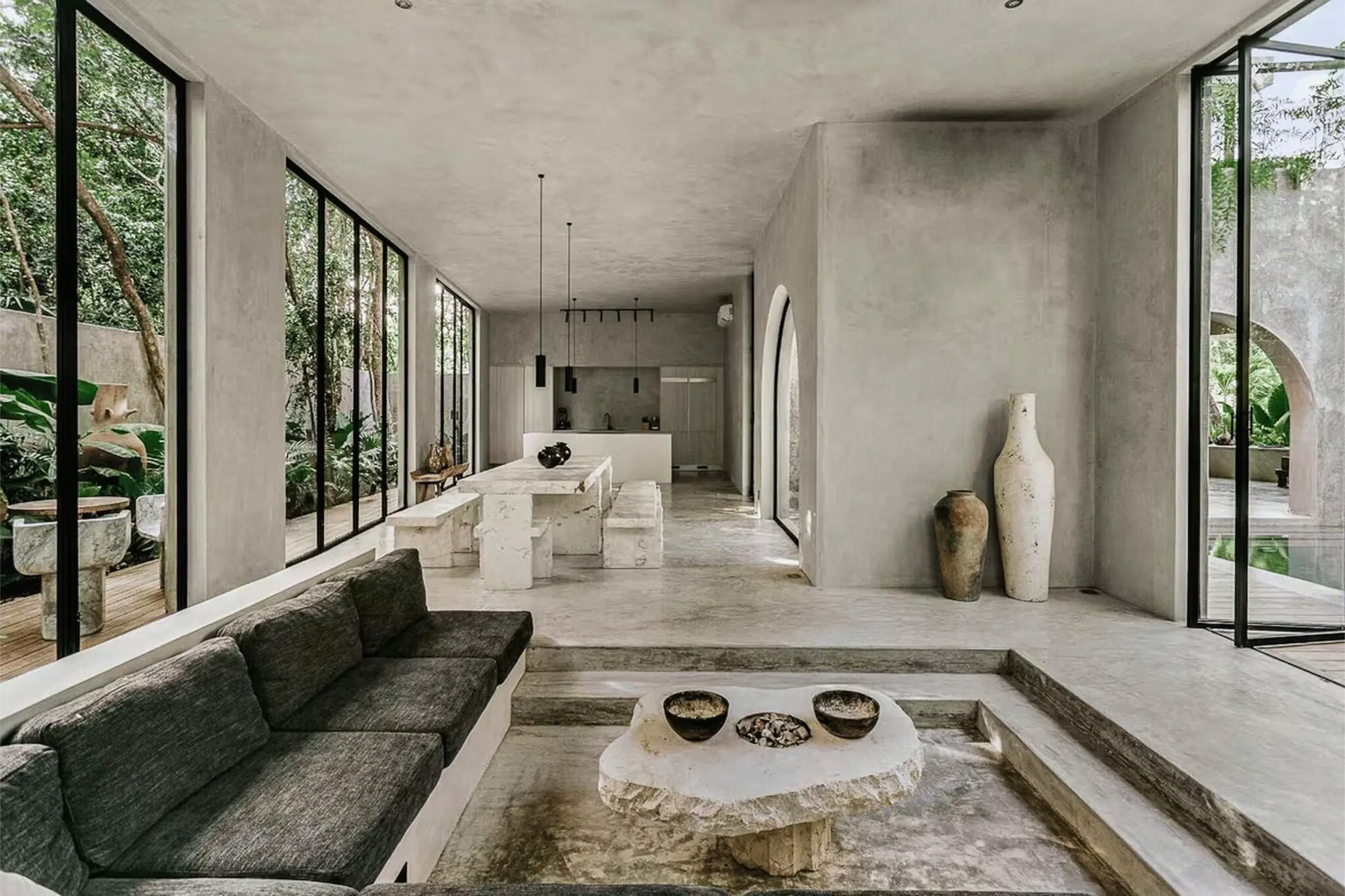Open-plan interior design featuring polished concrete floors, a sunken living area, and a stone dining table in Casa Shalva.