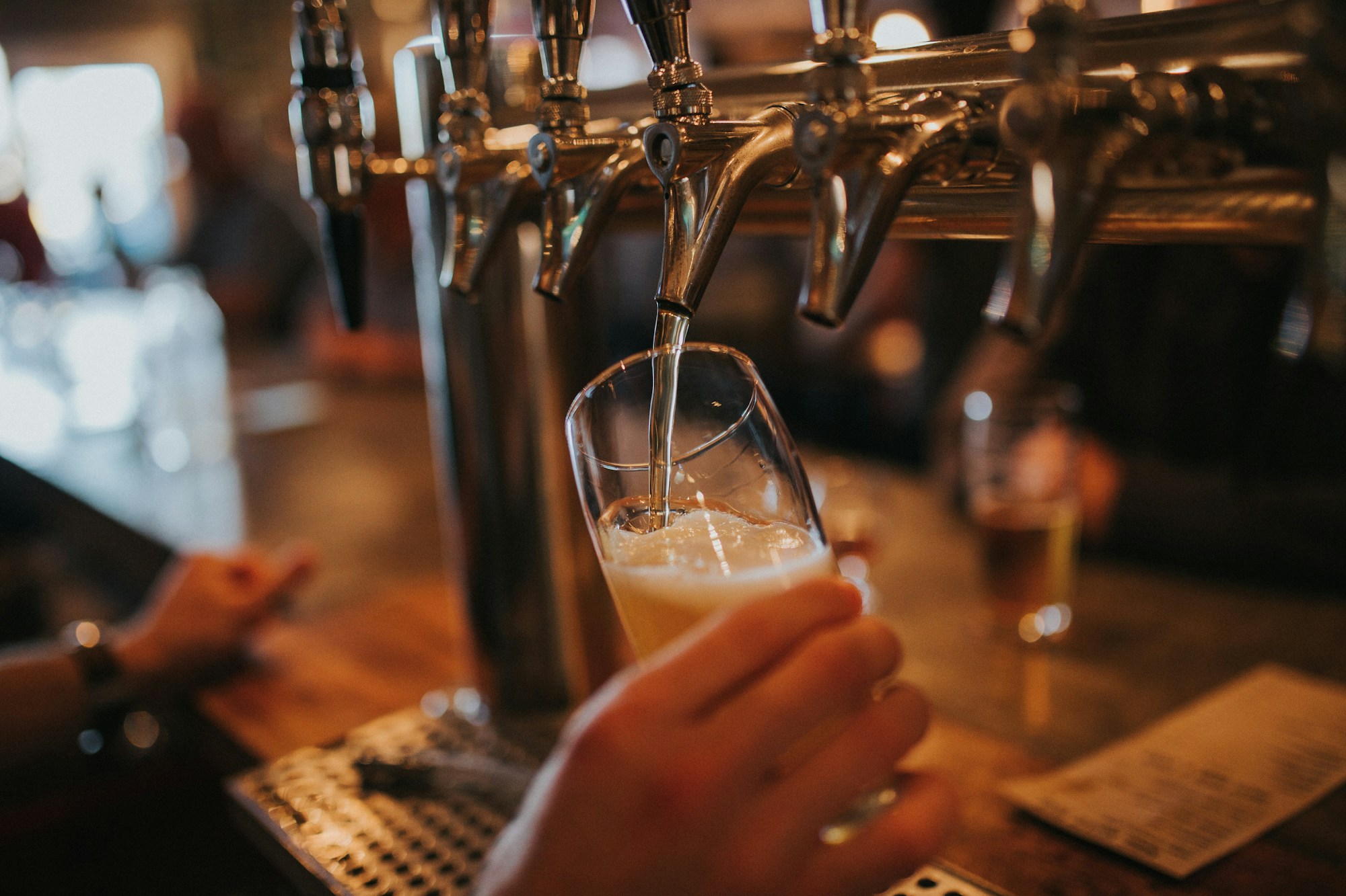 A bartender pouring a pale beer from a row of taps