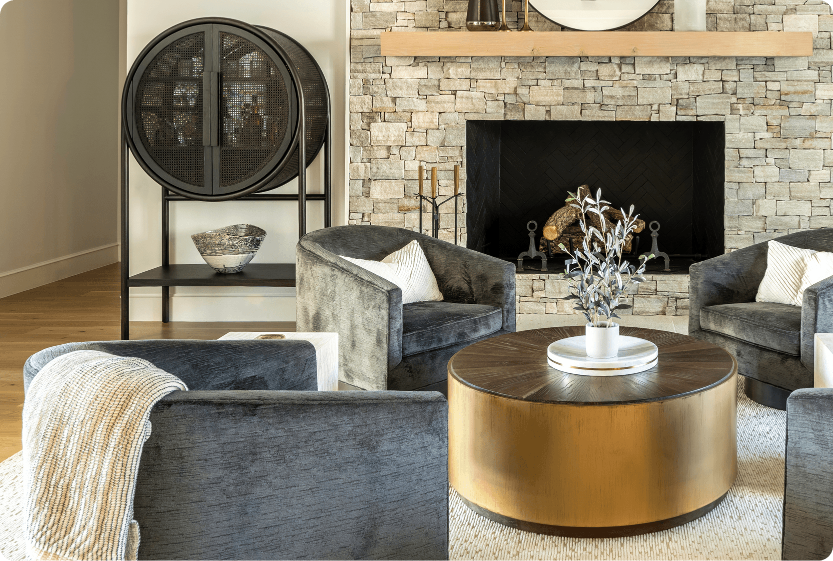 Modern sitting room with gray velvet armchairs, round brass coffee table, and natural stone fireplace wall