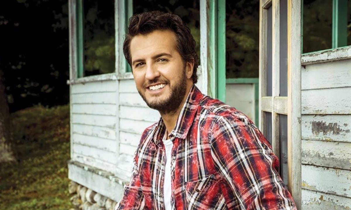 Man in red plaid shirt smiling outside rustic wooden building.