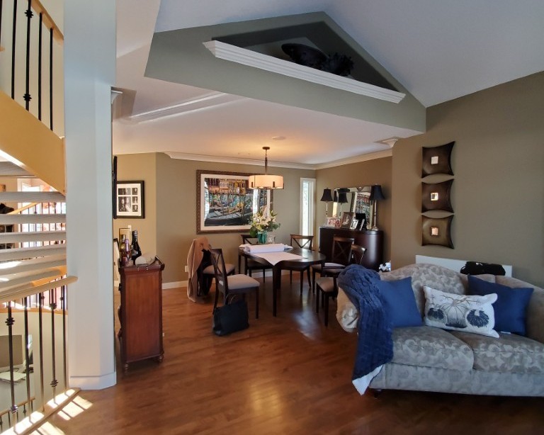 A dining area with furniture placed at an angle and things strewn about. The walls are olive/ taupe and make the room feel dark.