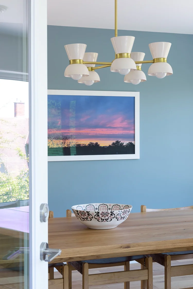 Modern two-story home with large glass windows, warmly lit interiors, and a balcony. Surrounded by trees and a manicured lawn at dusk. Cozy ambiance.