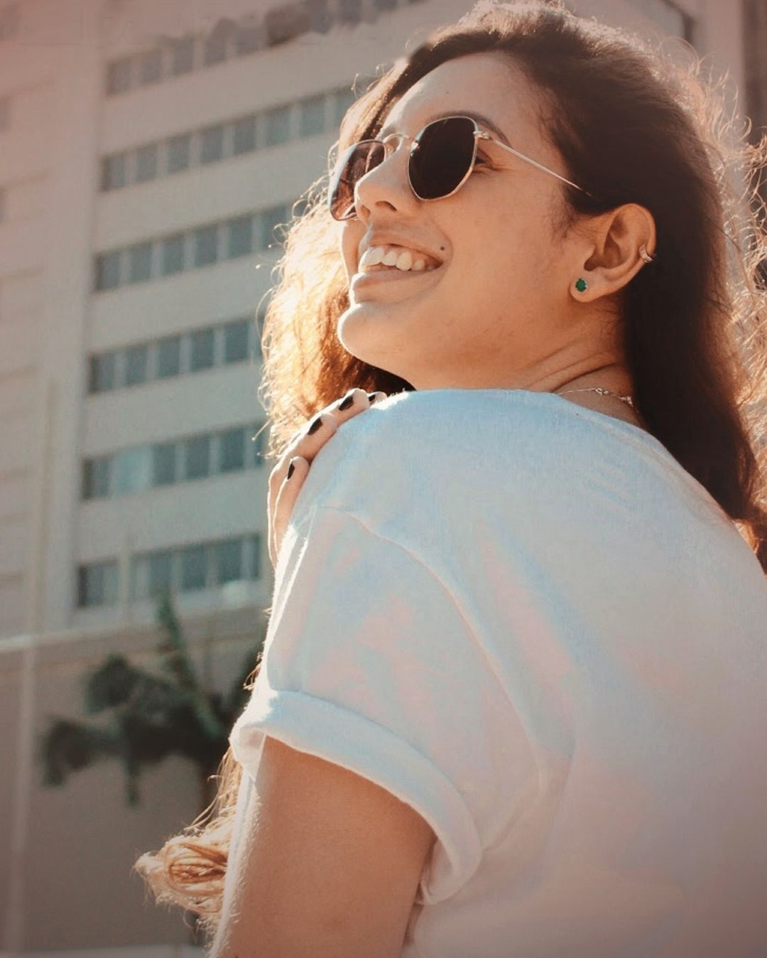 A woman in sunglasses smiling over her shoulder in the sun