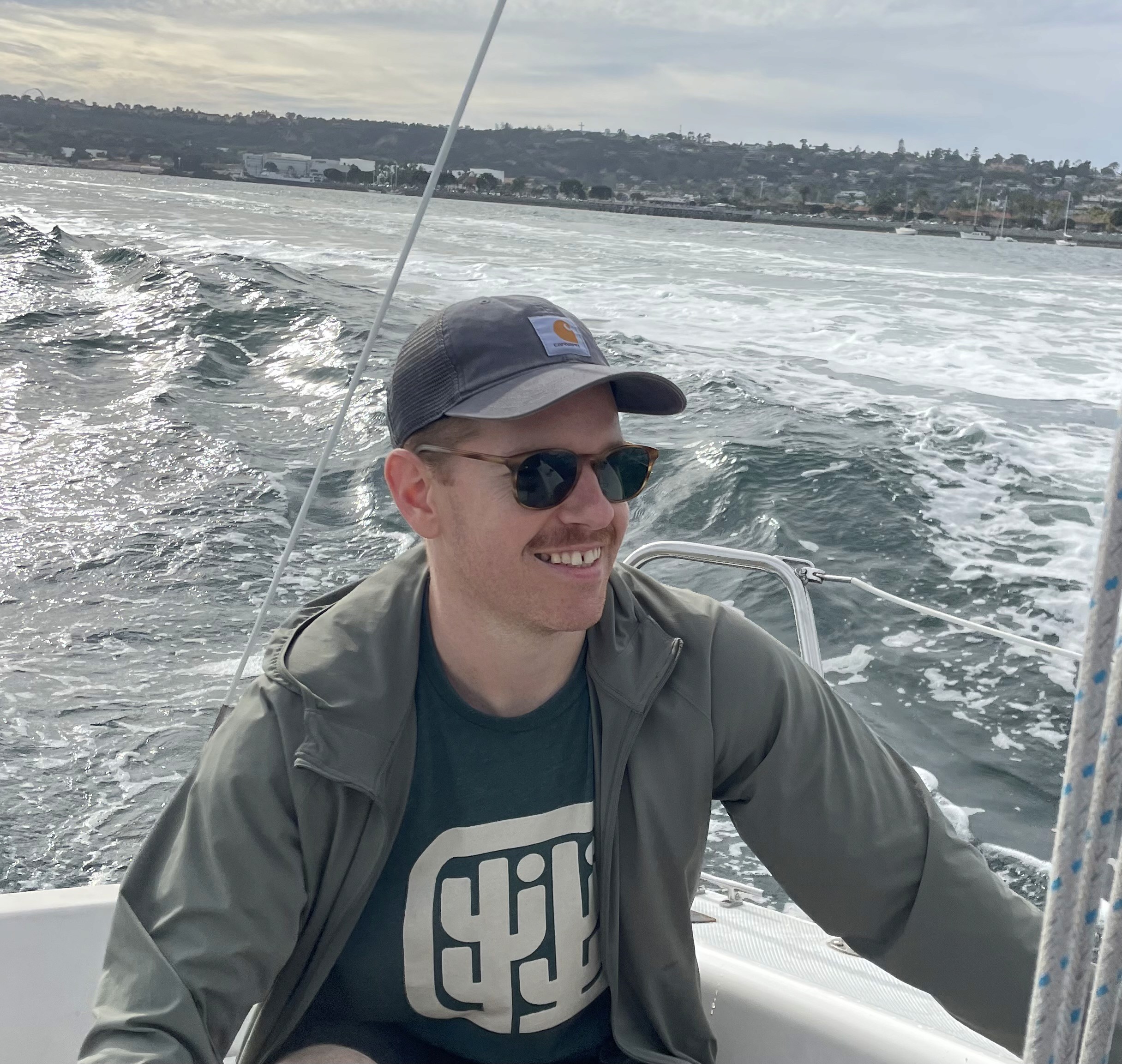 A person with wavy light hair stands facing slightly to the left, wearing a striped shirt against a neutral background.