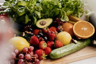 A variety of fresh fruits and vegetables arranged on a wooden surface, including grapes, oranges, and cucumbers.