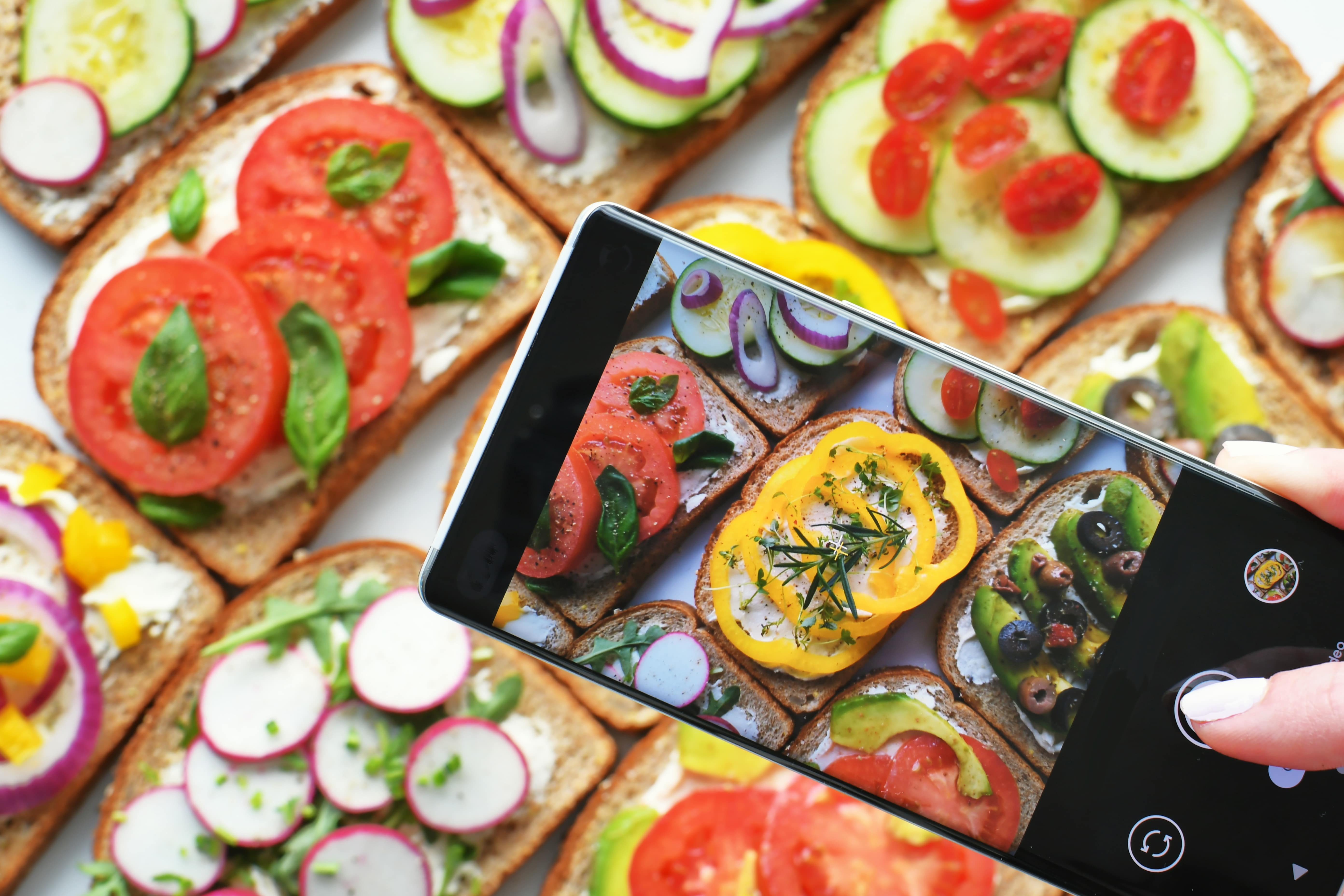 Close-up of a person photographing colorful vegetable toast with a smartphone for social media or food blogging.