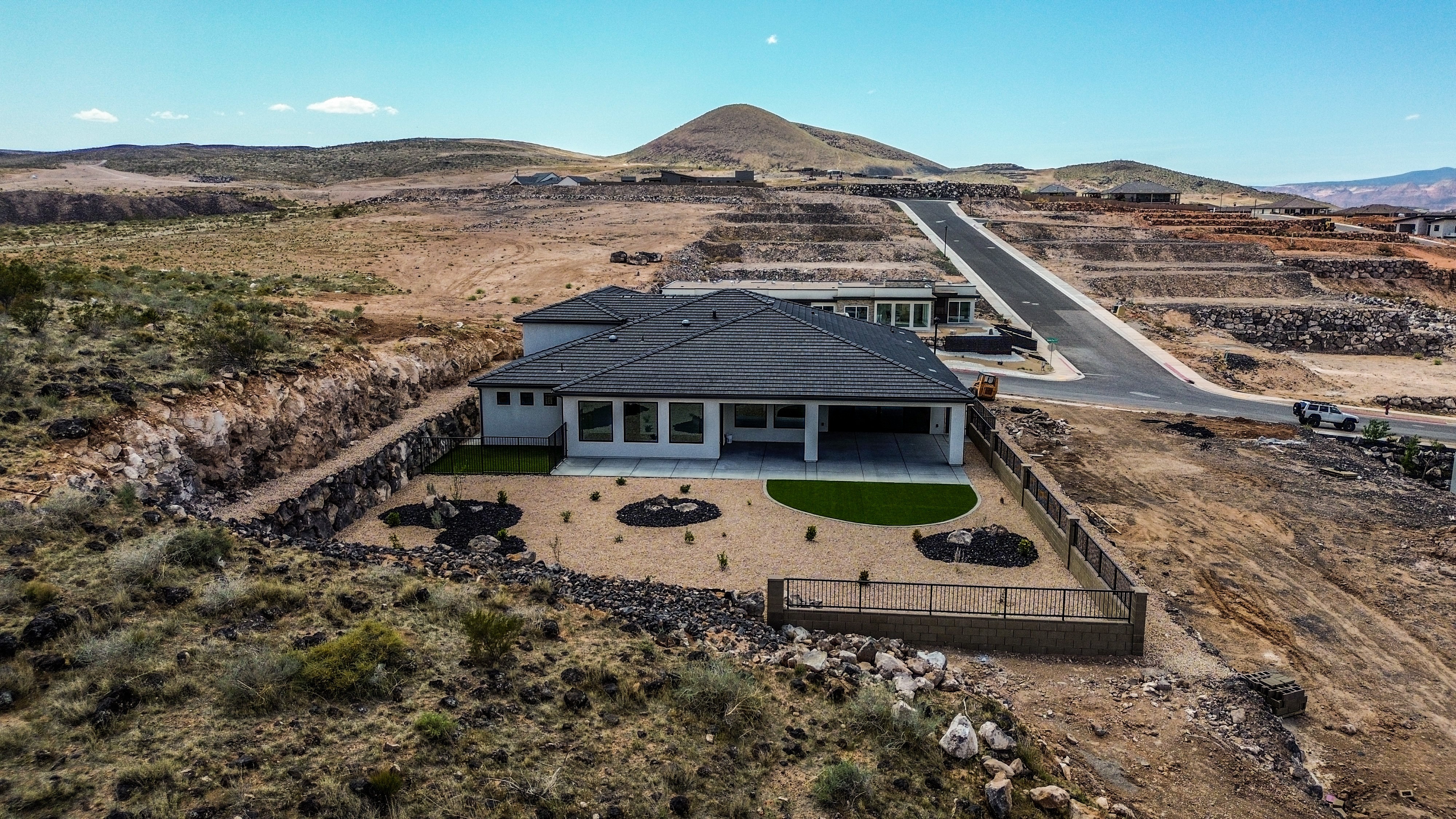 Aerial view of a Hurricane, Utah custom home with full landscaping, a stone and metal fence with natural land surrounding it.