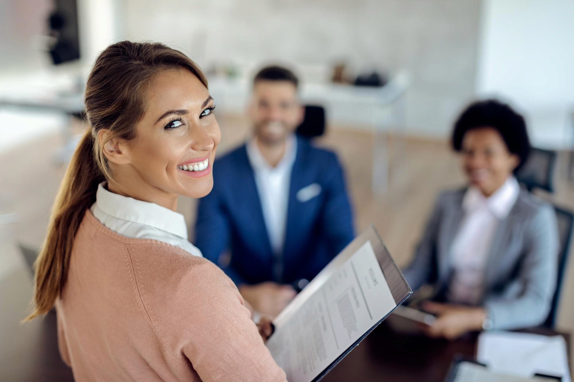 Recruiter smiling while holding documents in a meeting with two colleagues in the background.