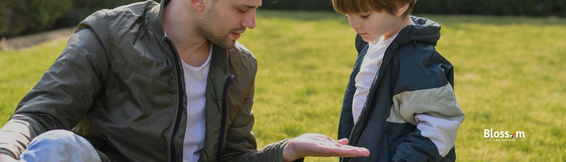 A father and son interacting outside, with the father showing something in his hand to the child.