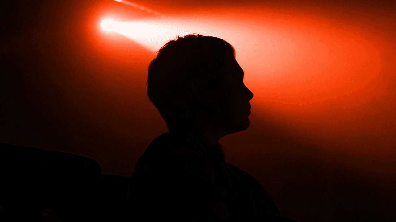 Man's silhouette in profile against a bright orange spotlight. Moody, dramatic lighting.