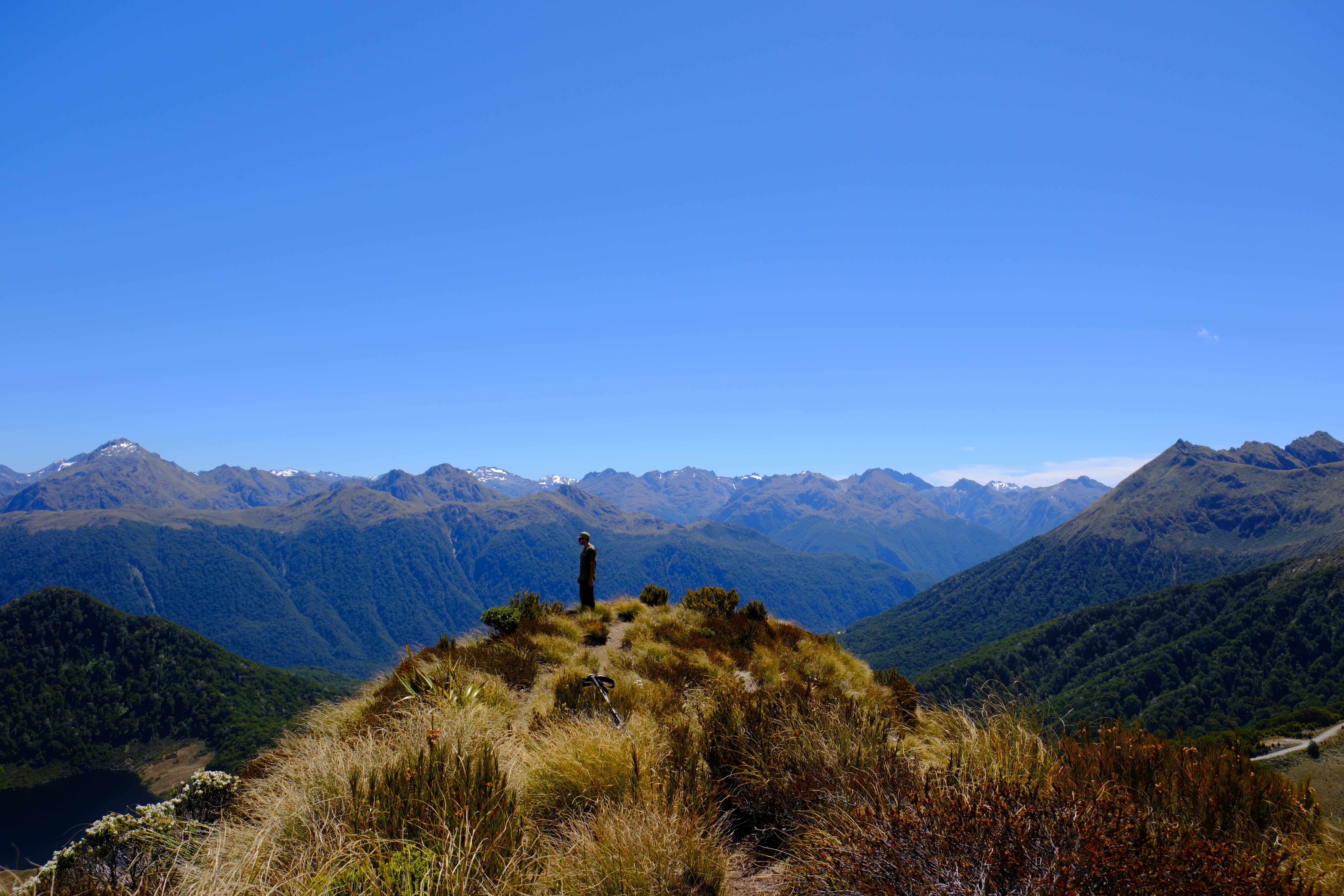 A lone hiker on a sunlit grassy ridge with mountain valleys beyond