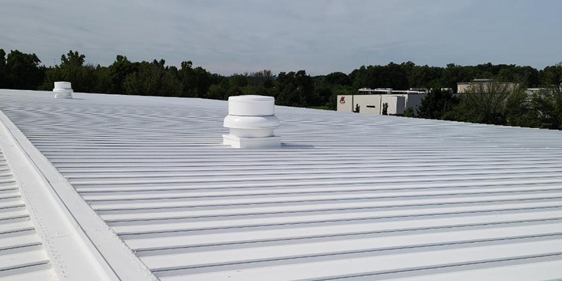 Large commercial metal building with a bright white acrylic roof coating, reflecting sunlight to improve energy efficiency and protect against weather damage.