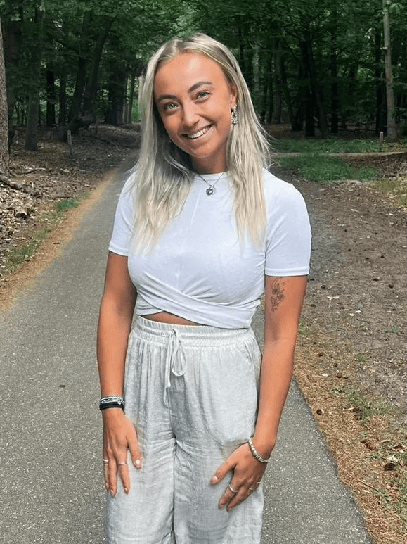 Smiling female therapist with short gray hair, wearing a brown top and a purple shawl, surrounded by a cozy background.