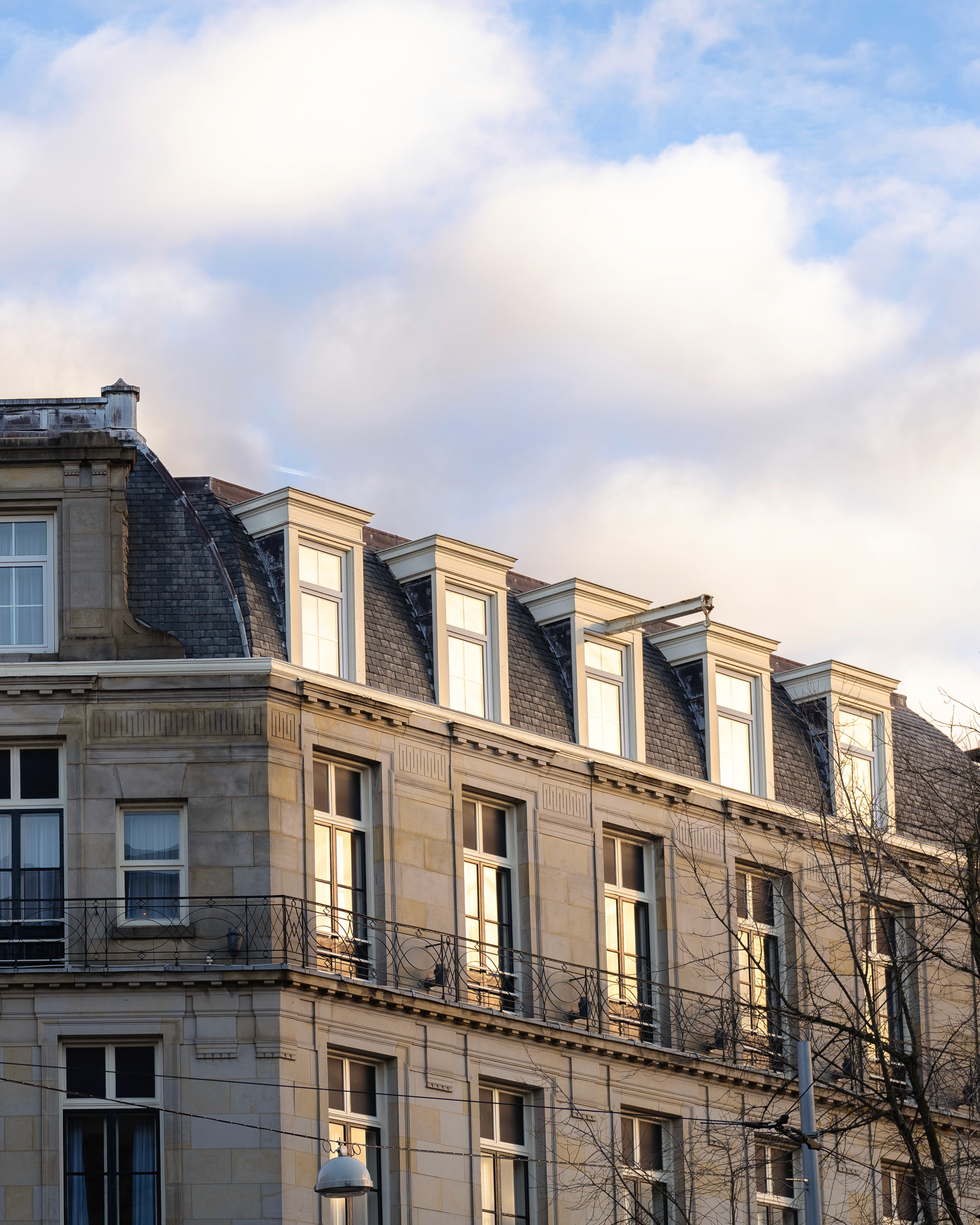 Detail of a top-floor Amsterdam canal house, with yellow sun rays making it pop against the blue sky.