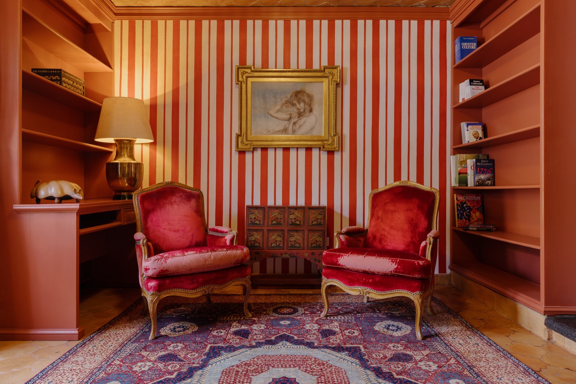 Upstairs sitting room with red velvet armchairs, striped wallpaper, built-in shelves, and vaulted brick ceiling at La Residencia.