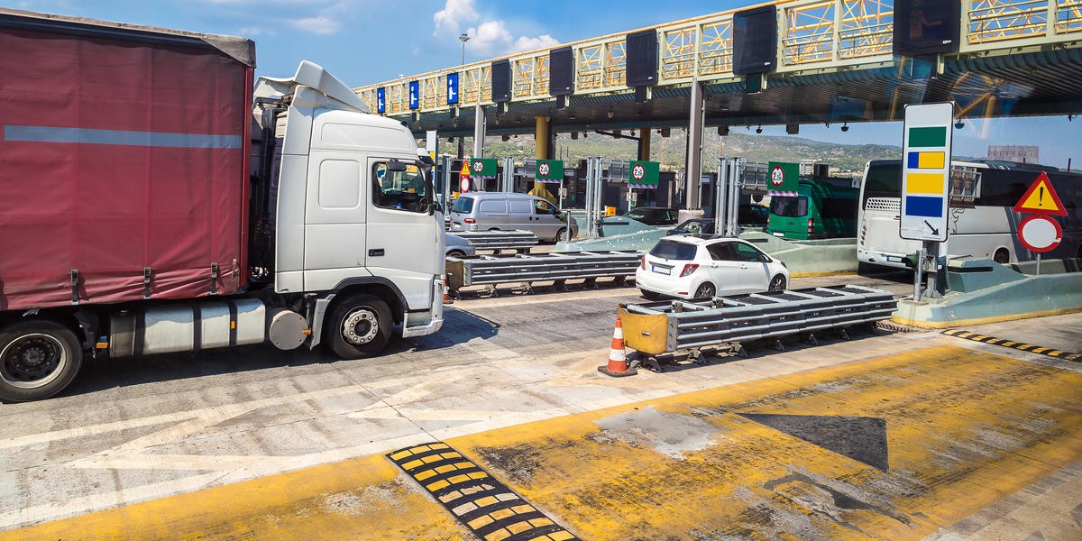 Several freight trucks traveling on a highway approaching a toll station in Europe.