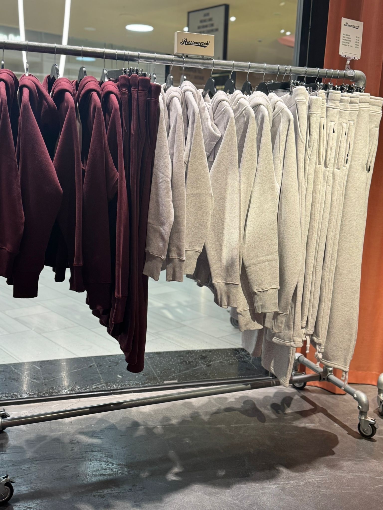 Clothing rack with maroon red and light grey Russemerch garments on hangers