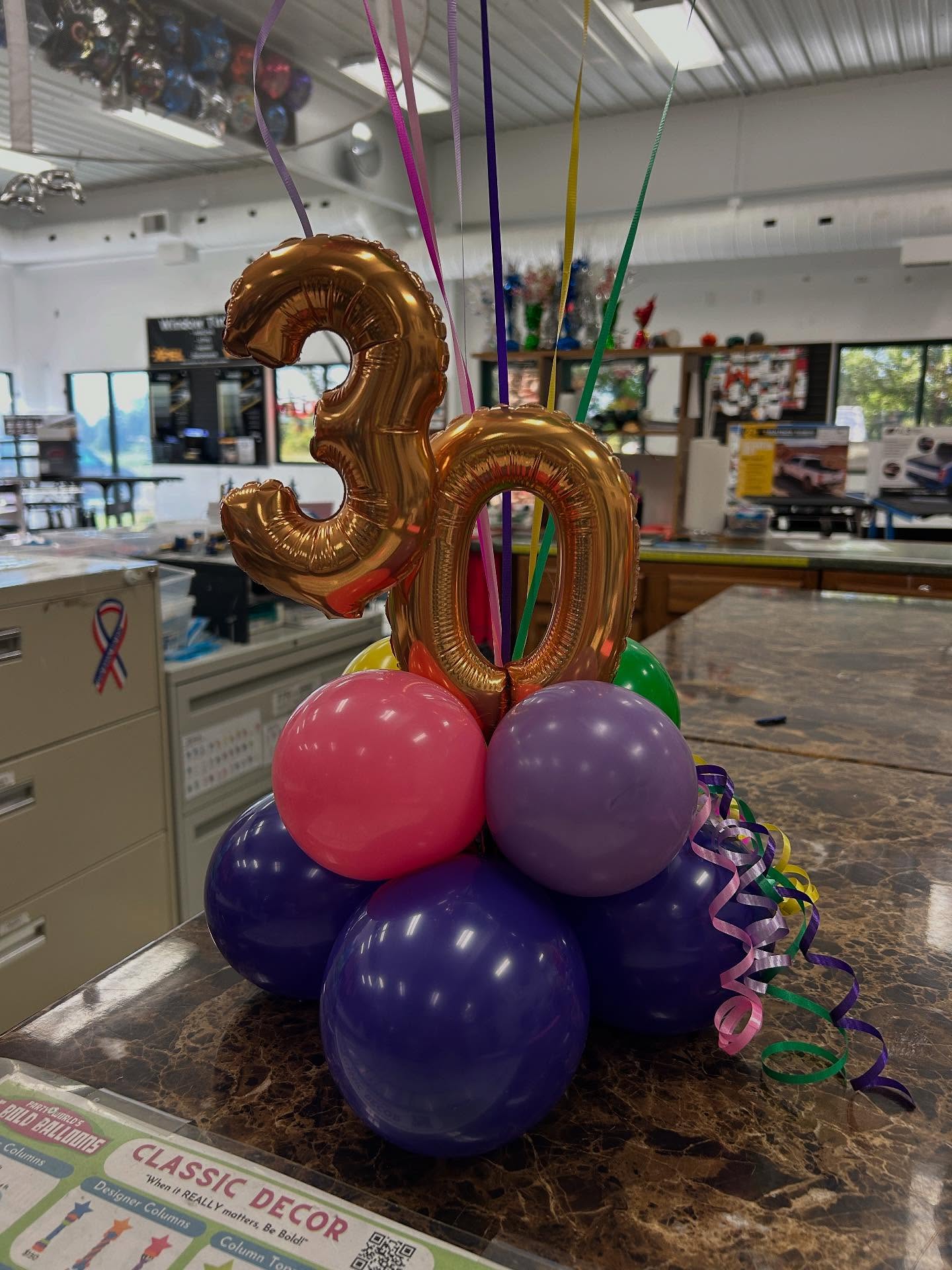 Colorful number 30 balloon centerpiece with gold topper and purple, red, and orange balloon base designed by Be Bold Balloons