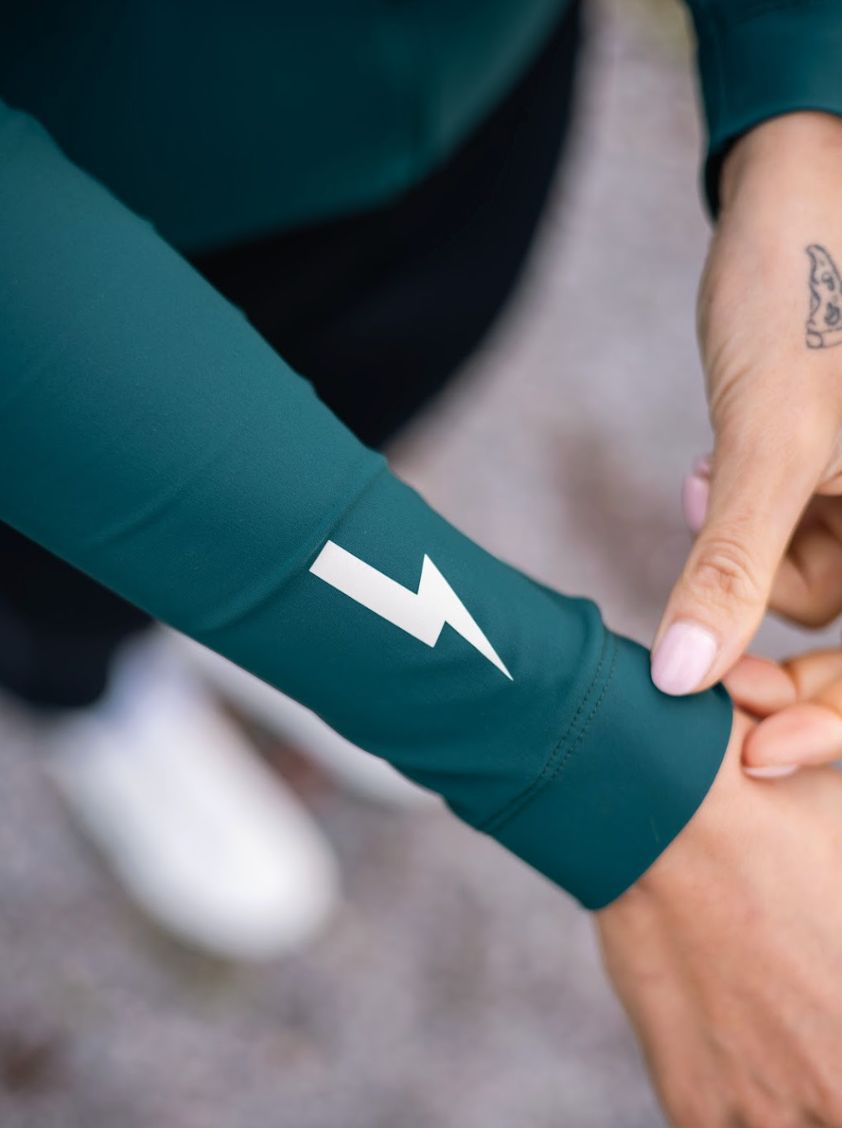 Close-up-of-the-sleeve-cuff-of-a- teal-long-sleeve-cycling-top- showing-the-white-lightning-bolt- graphic-near-the-wrist