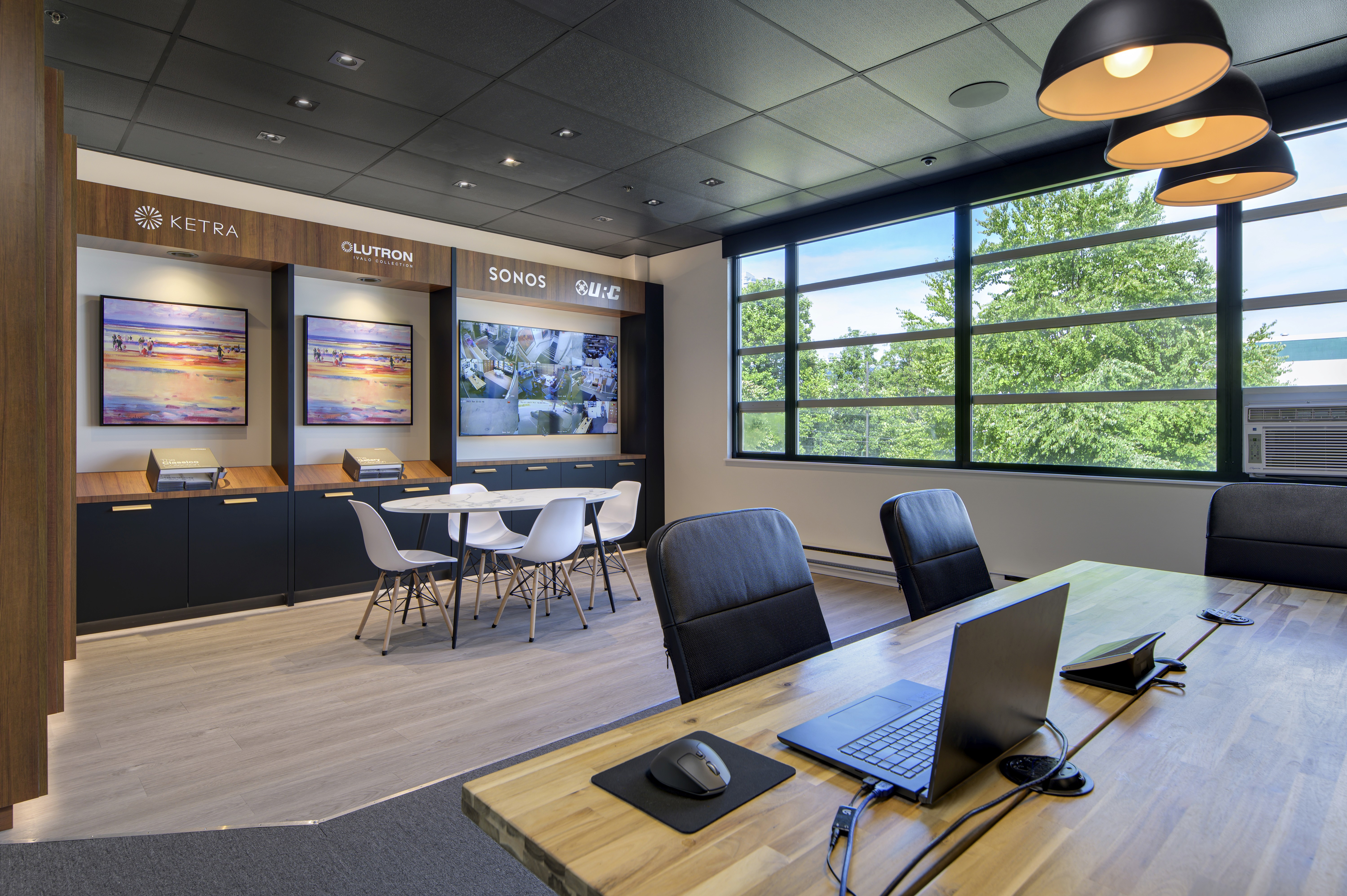 Modern demo office space with a wooden conference table, black guest chairs, and a wall display of smart-home panels beneath large industrial-style windows.