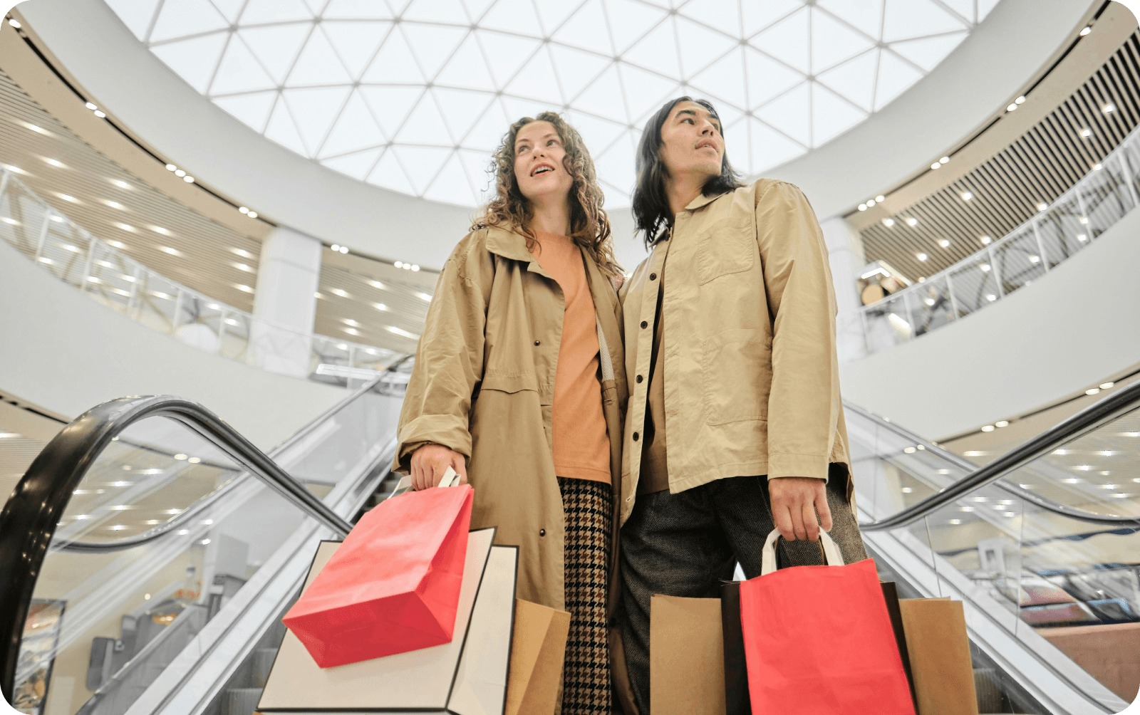 Couple on an escalator in a mall, holding shopping bags.