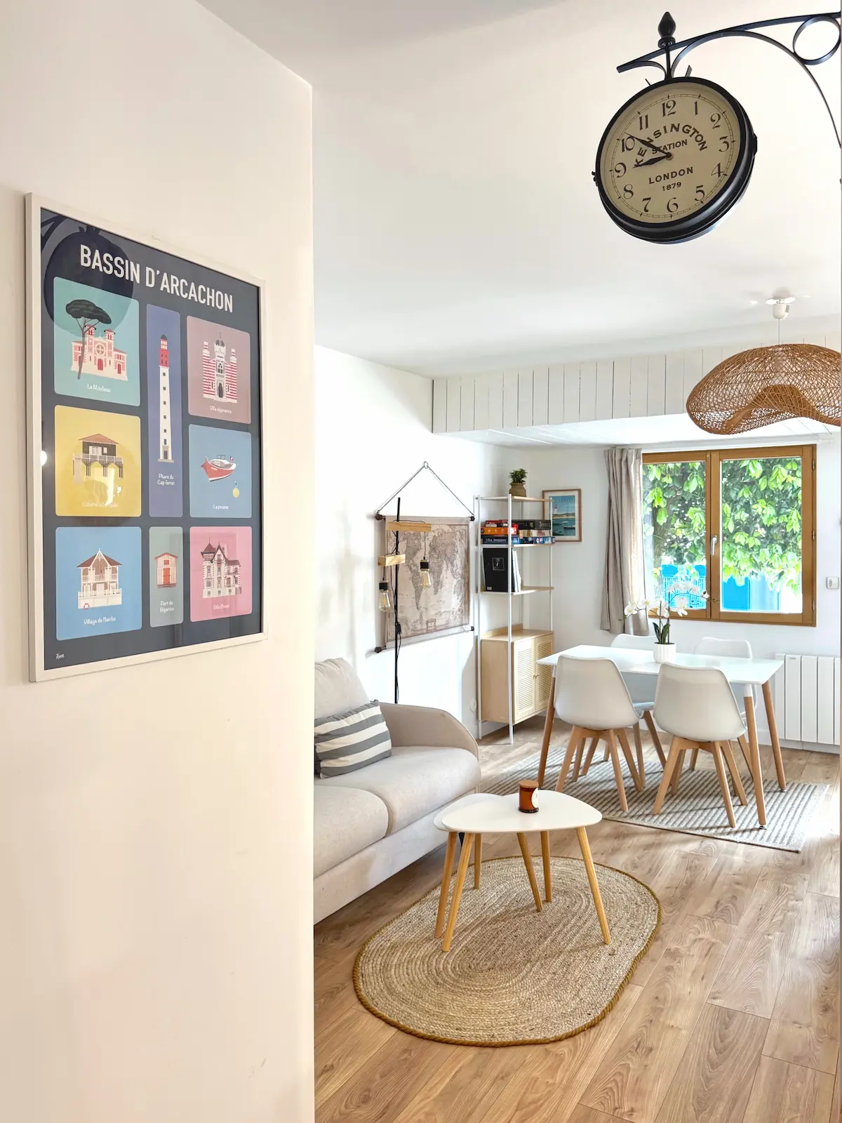 Salon lumineux avec affiche vintage, canapé et suspension en rotin – Andernos-les-Bains.