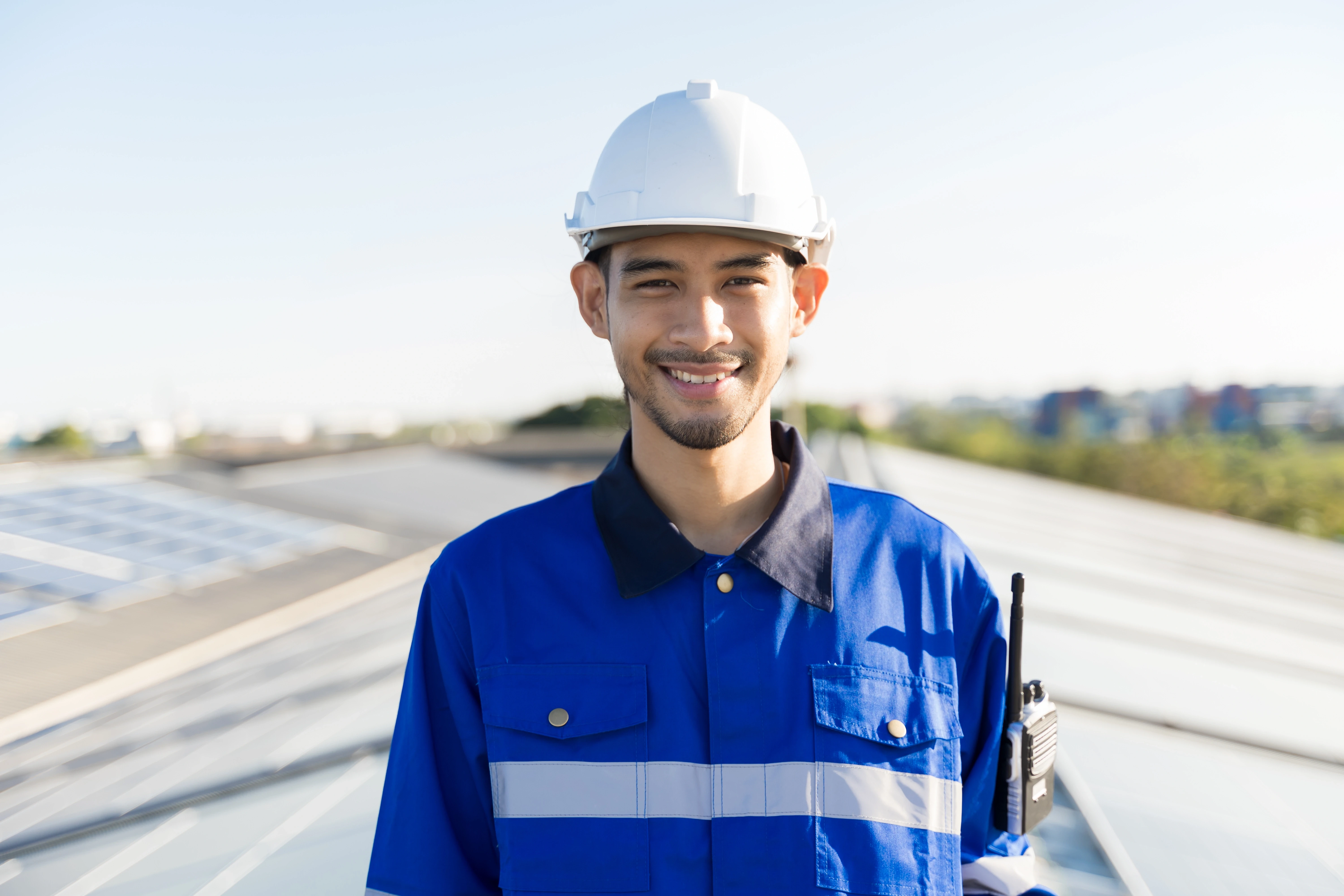 Freundlicher Solarberater in Schutzhelm lächelt auf dem Dach vor Solarpaneelen, symbolisiert Fachkompetenz und Kundenservice im Bereich Photovoltaikanlagen.