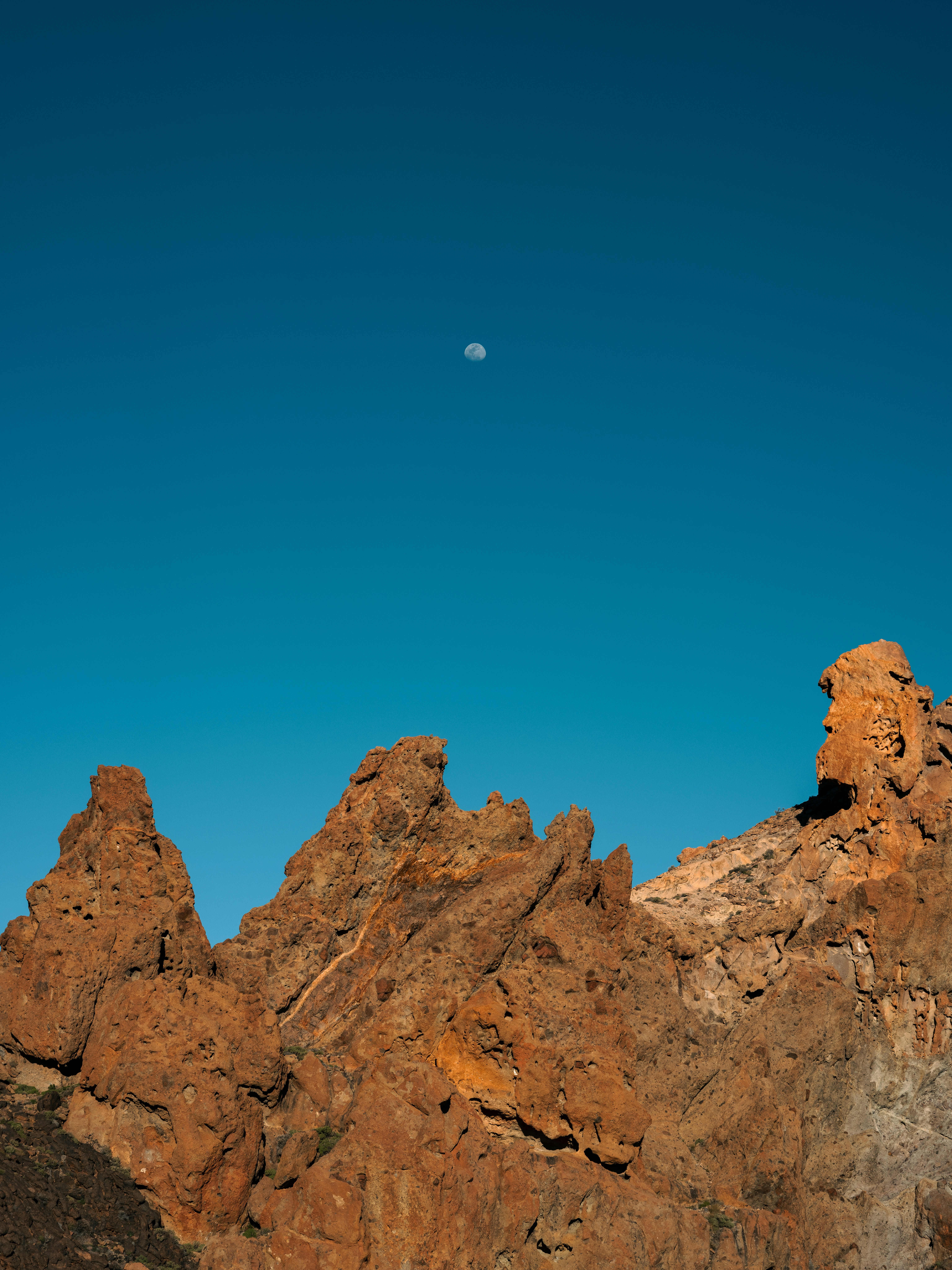 Rocky mountain peaks under a clear blue sky with moon.