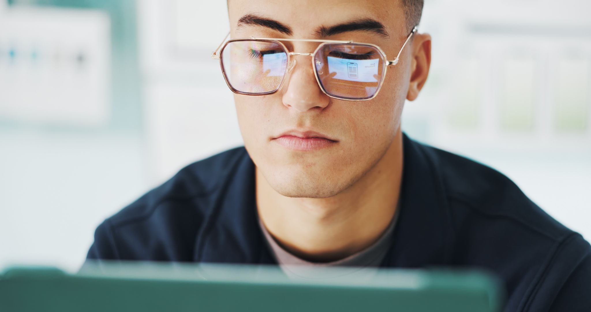 Professional wearing glasses working on laptop with screen reflection visible in lenses.